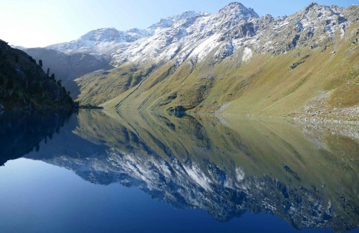 Panoramablick auf den malerischen Cleuson-See in Nendaz, Schweiz, umgeben von schneebedeckten Bergen und spiegelndem, klarem Wasser. Nendaz ist bekannt für seine vielfältigen Sommeraktivitäten wie Wandern, Mountainbiken und Abseilen, und wird im Blogpost '5 Orte für schöne Sommerferien in der Schweiz' als einer der Top-Ferienorte hervorgehoben. Weitere empfohlene Ferienorte sind Pays-d'Enhaut, Bellwald, Heidiland und Vallée de Joux, die alle eine Vielzahl von Aktivitäten für Familien, Paare, Abenteurer und Ruhesuchende bieten.