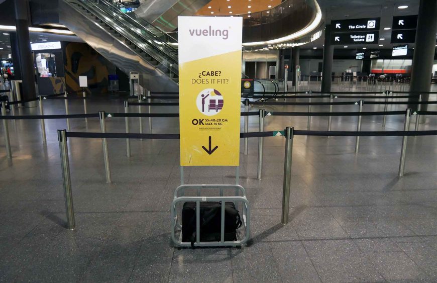 Praktischer Rucksack für Flugreisen in einer Grössenkontrolleinheit am Flughafen. Das Schild von Vueling zeigt die zulässigen Abmessungen von 55x40x20 cm und das maximale Gewicht von 10 kg. Der Rucksack passt perfekt in die Metallrahmen-Vorrichtung, was bestätigt, dass er den Handgepäckbestimmungen entspricht. Im Blogbeitrag geht es darum, warum ein praktischer Rucksack für Flugreisen unverzichtbar ist, welche Merkmale er aufweisen sollte und welche Modelle besonders empfehlenswert sind.