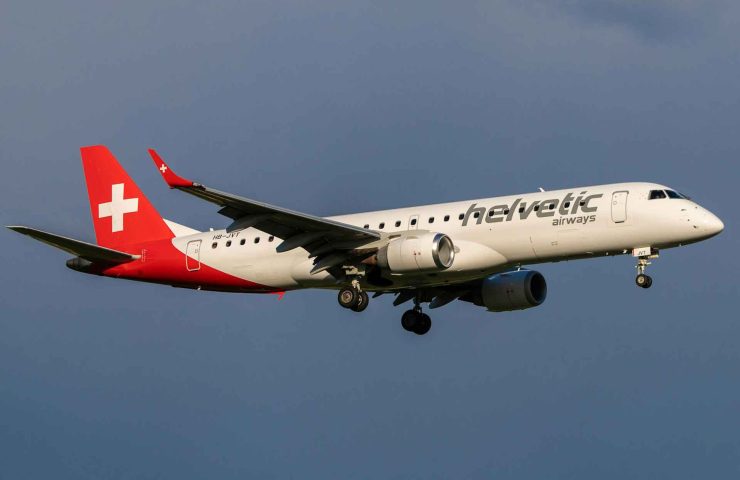 Bild eines Helvetic Airways Flugzeugs vom Typ Embraer 190 in der Luft, mit der charakteristischen roten Heckflosse und dem Schweizer Kreuz, sowie dem Schriftzug 'Helvetic Airways' auf dem Rumpf. Der Blogpost behandelt ausführlich die Gepäckrichtlinien bei Helvetic Airways, einschließlich detaillierter Informationen zu den Handgepäckbestimmungen wie Grösse, Gewicht und erlaubte Gegenstände. Zudem werden die Regeln für Aufgabegepäck, Sondergepäck wie Sportausrüstung und Fahrräder, sowie die Beförderung von Tieren erläutert. Der Beitrag gibt hilfreiche Tipps, um Übergepäckgebühren zu vermeiden und informiert über spezielle Regelungen für Flüssigkeiten und medizinische Ausrüstungen.