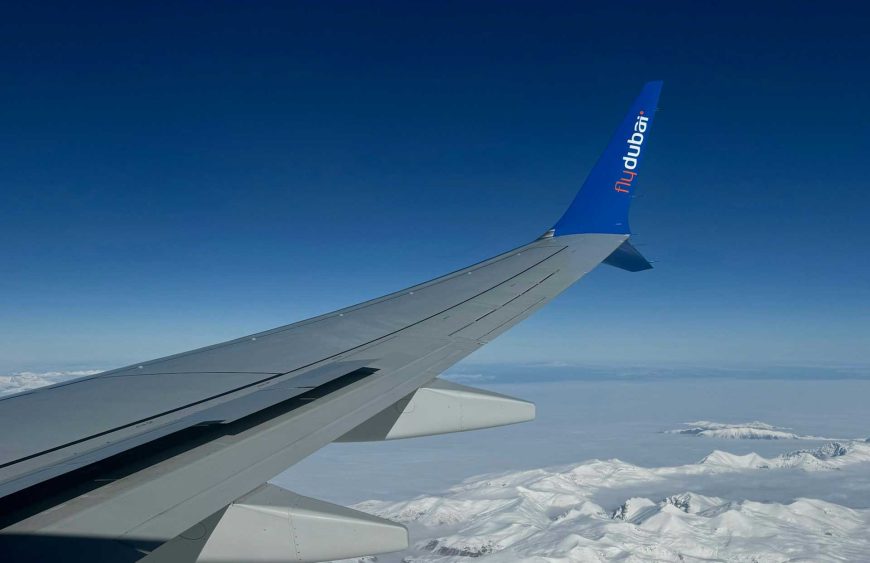 Der Flügel eines flydubai Flugzeugs, aufgenommen während des Flugs über eine weite, schneebedeckte Berglandschaft. Der Flügel zeigt das markante flydubai Logo in Blau und Orange auf dem Winglet, während sich unter dem Flugzeug die schroffen, weißen Gipfel erstrecken, die im Kontrast zu dem tiefblauen Himmel stehen. Das Bild vermittelt die Ruhe und Weite eines Flugs in großer Höhe und symbolisiert das Reisen mit flydubai. Im Blogartikel werden detaillierte Informationen zu den Gepäckbestimmungen, insbesondere zum flydubai Handgepäck, gegeben. Diese sollen den Lesern helfen, optimal für ihre Reise mit der Airline vorbereitet zu sein, indem sie die Vorgaben für Hand- und Freigepäck genau kennen.