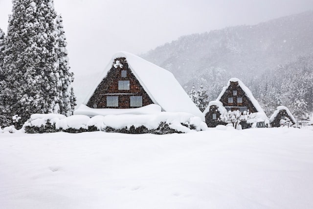 Verschneite traditionelle Häuser im Dorf Shirakawa-go in Japan, einem UNESCO-Weltkulturerbe, das für seine markanten Gassho-zukuri-Bauweise bekannt ist. Die Häuser haben steil geneigte Strohdächer, die dick mit Schnee bedeckt sind und sich harmonisch in die winterliche Alpenlandschaft einfügen. Die Szene vermittelt eine ruhige, idyllische Atmosphäre, die typisch für dieses historische Dorf ist und besonders Fotoliebhaber während der Wintermonate auf einer Japan Rundreise anzieht.